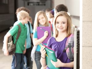 A waist up image of a group of middle school age students talking at their lockers during a break from class.